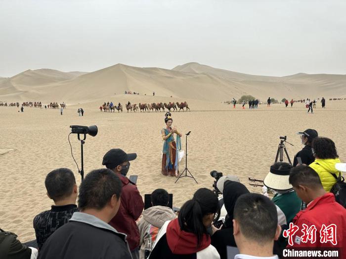 圖為2023年4月底，敦煌大漠“逐舞者”奧楠在鳴沙山月牙泉景區(qū)視頻直播，吸引游人圍觀?！●T志軍 攝